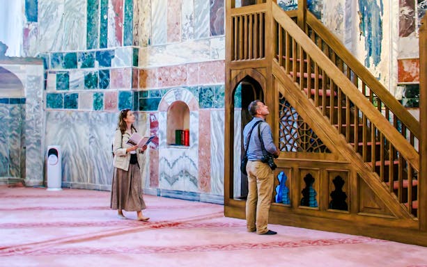 Guests exploring the interior of Kariye Mosque, Istanbul, near ornate wooden staircase.