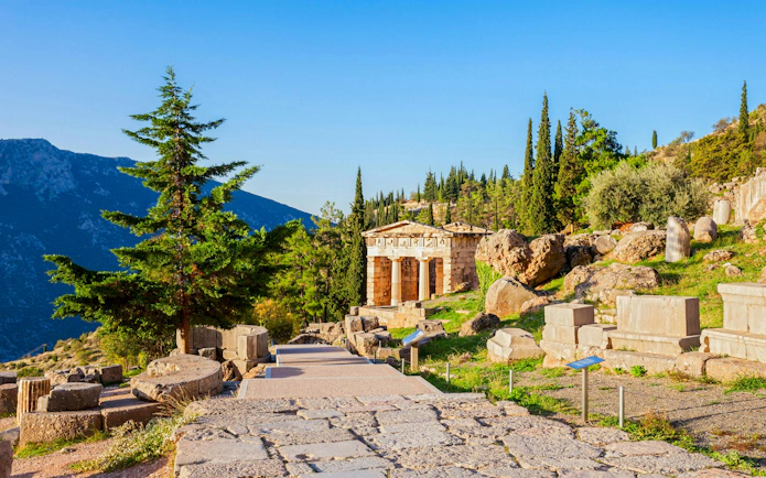 Ancient ruins at Delphi Sanctuary, Greece, with mountainous backdrop.