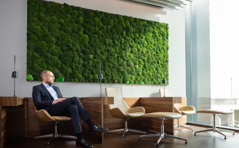 Man sitting in BER Lounge Tegel at Berlin Brandenburg Airport with green moss wall and modern seating.