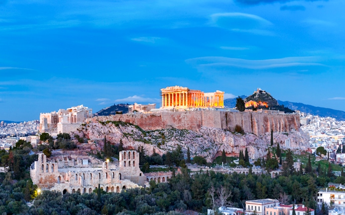 Acropolis illuminated at night during Athens panoramic tour with open double-decker bus.