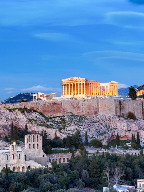 Acropolis illuminated at night during Athens panoramic tour with open double-decker bus.