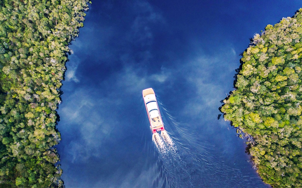 Aerial view of a boat cruising on Gordon River, surrounded by lush greenery, Tasmania.