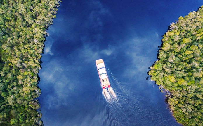 Aerial view of a boat cruising on Gordon River, surrounded by lush greenery, Tasmania.
