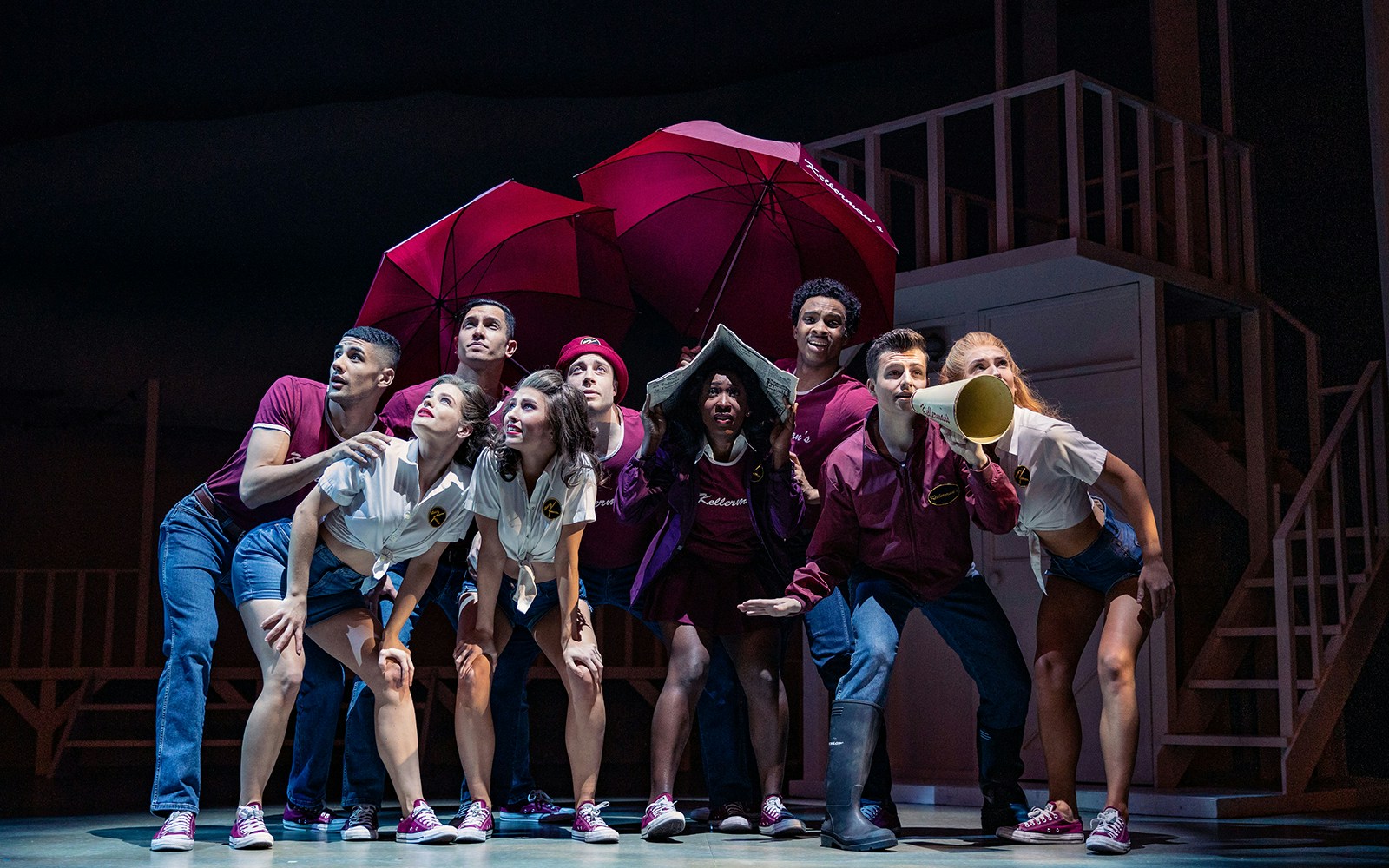 Performers on stage in a scene from Dirty Dancing musical, holding red umbrellas.