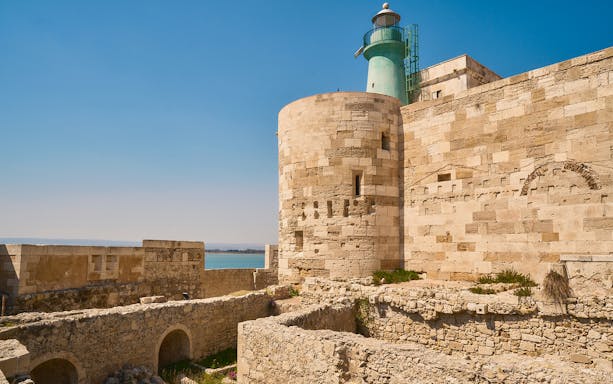 Maniace Castle stone walls and lighthouse overlooking the sea in Syracuse, Italy.