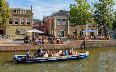 Boat tour on Groningen canal with people enjoying outdoor cafes along the waterfront.