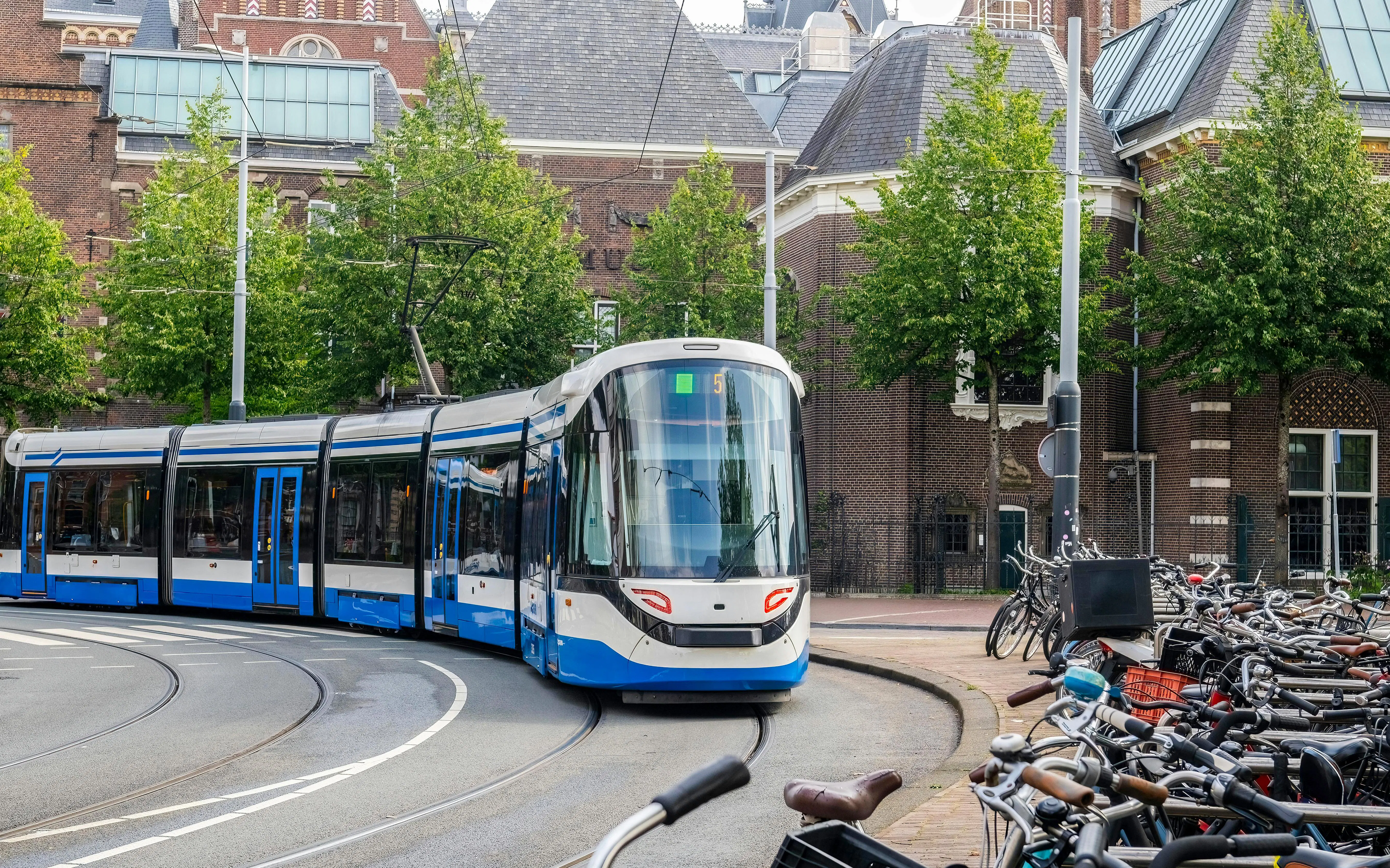 Amsterdam tram on a curved track near historic buildings and parked bicycles.