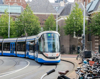 Amsterdam tram on a curved track near historic buildings and parked bicycles.