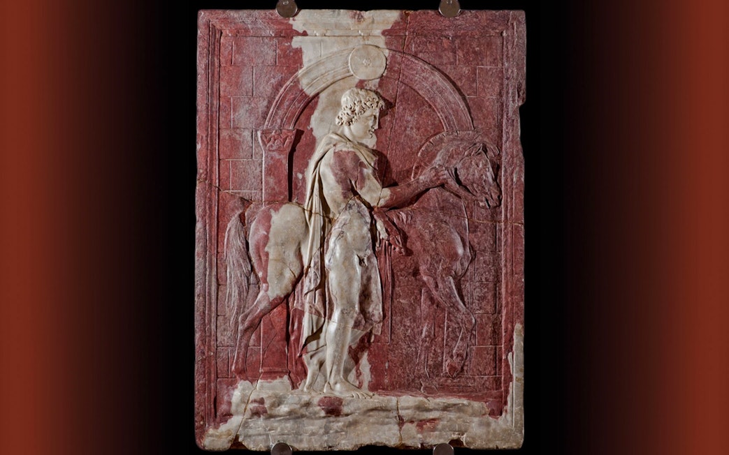 Roman marble relief of a Dioscuro with horse in front of a city gate.