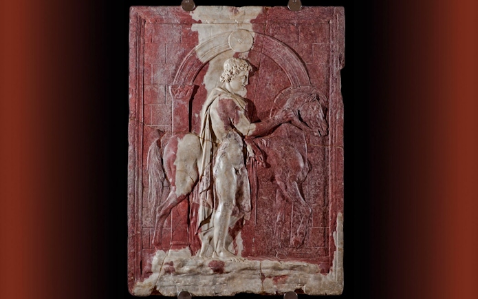 Roman marble relief of a Dioscuro with horse in front of a city gate.