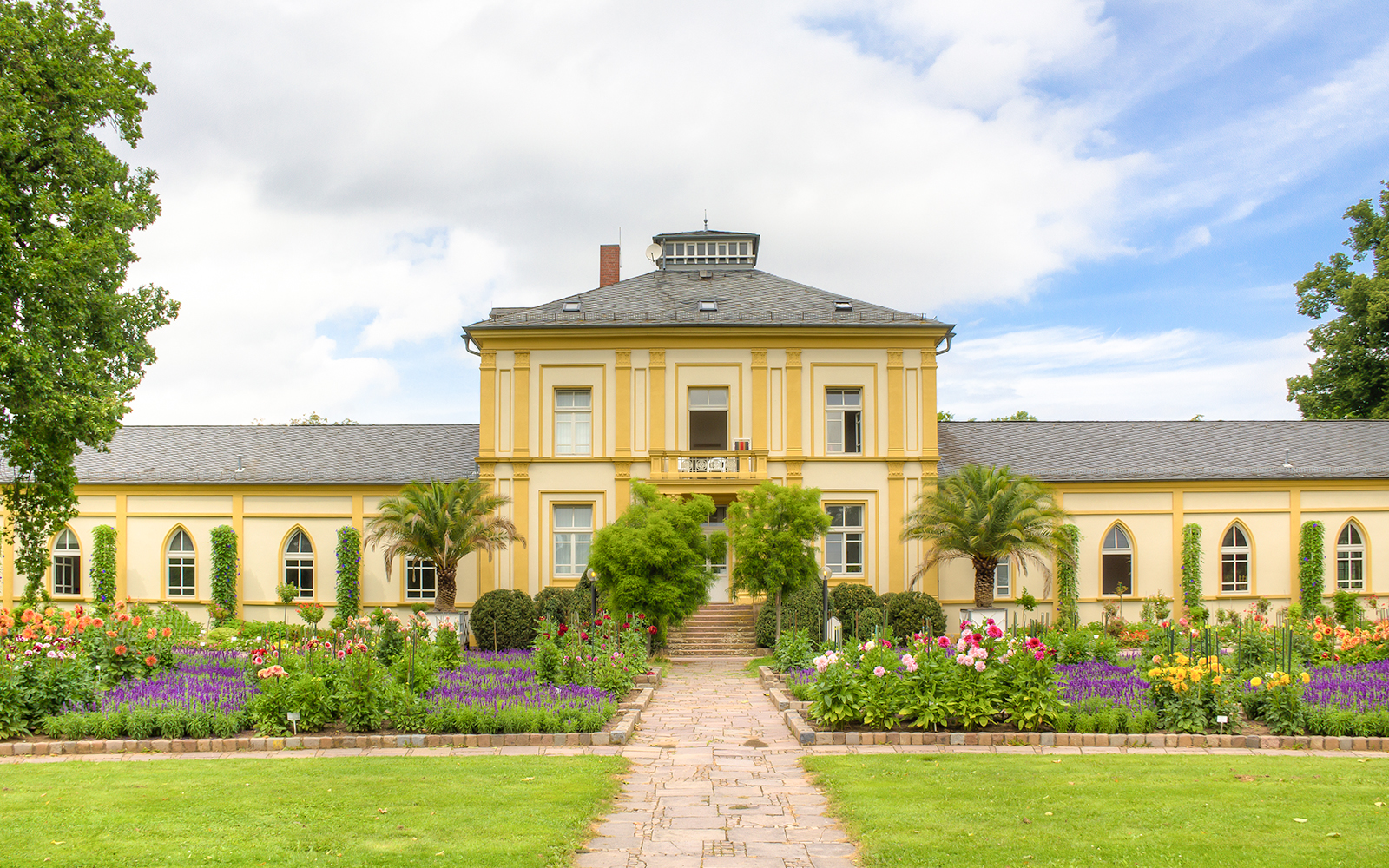A yellow building with beautiful flowers blooming in the garden, PalmGarten