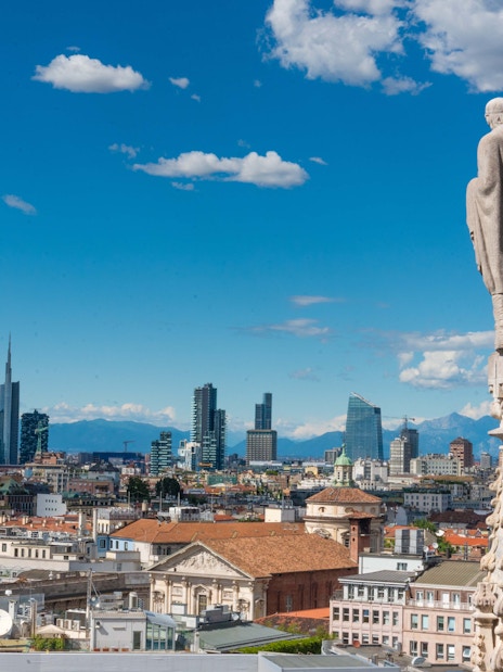 Rooftop view of Milan cityscape from Duomo with skyline and mountains.