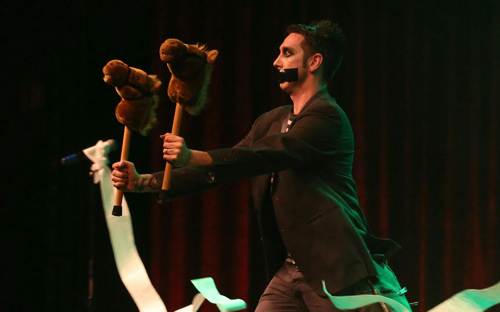 Performer with tape on mouth holding hobby horses during Tape Face show in Las Vegas.