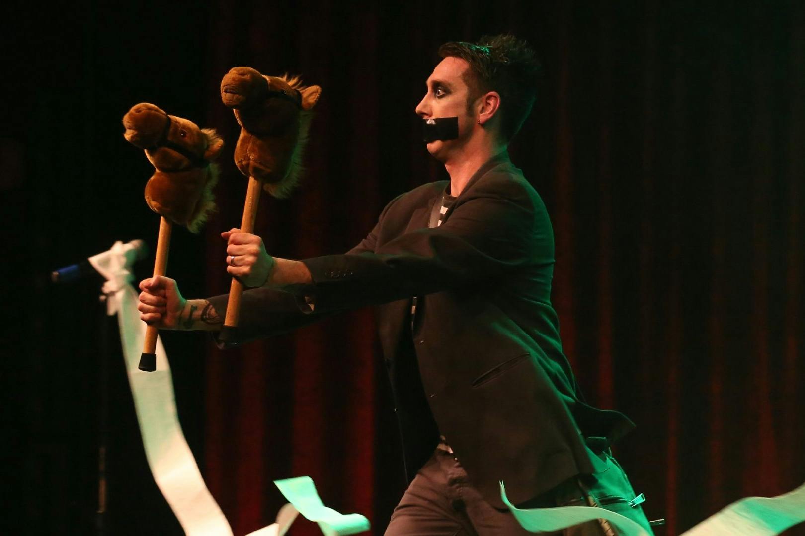 Performer with tape on mouth holding hobby horses during Tape Face show in Las Vegas.