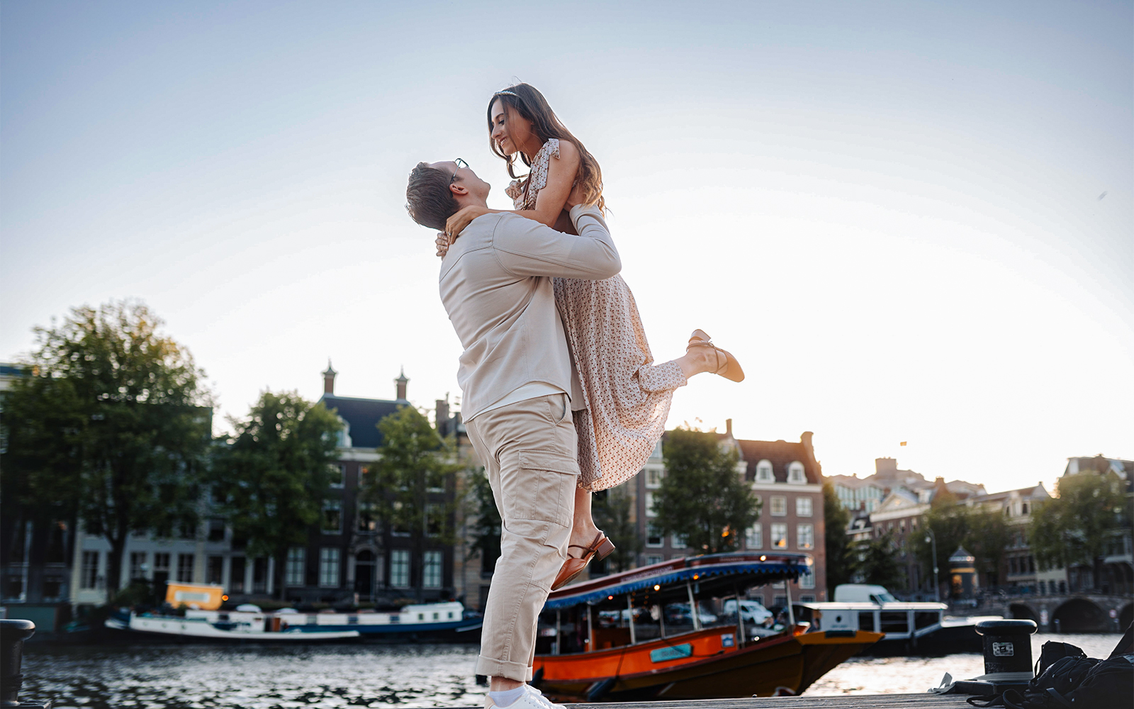 Couple posing near Magere Brug in Amsterdam with canal and boats in background.