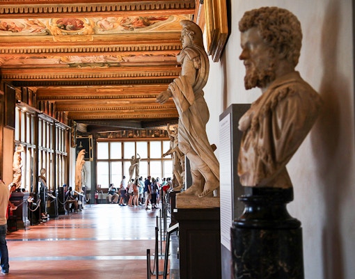 Visitors stroll through the Uffizi Gallery's Hall of Statues, Florence, immersed in historic art, available through timed entry tickets