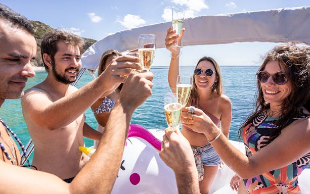Friends toasting with champagne on a private boat in the ocean.