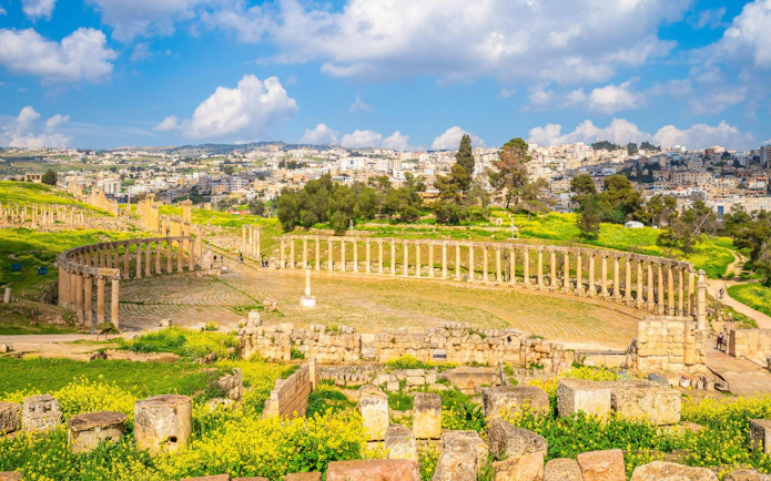 Oval Forum and Cardo Maximus ruins in Jerash, Jordan with cityscape in the background.