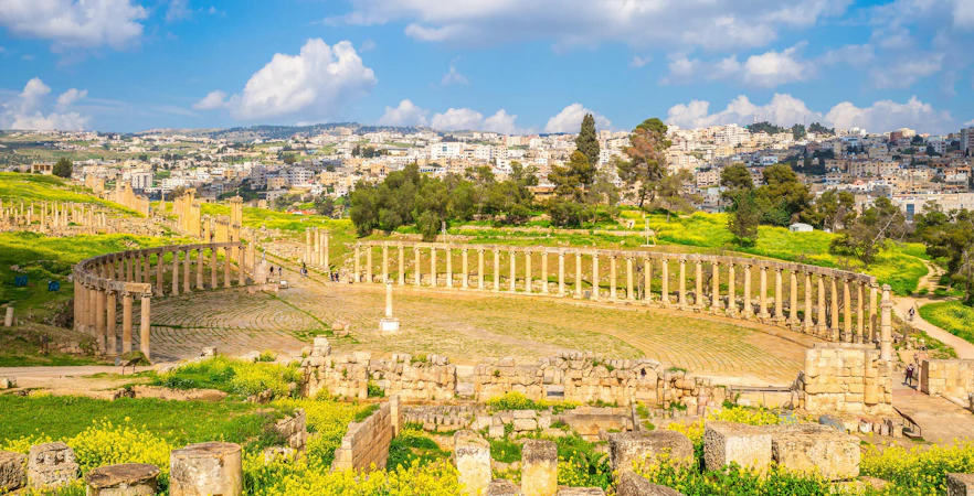 Oval Forum and Cardo Maximus ruins in Jerash, Jordan with cityscape in the background.