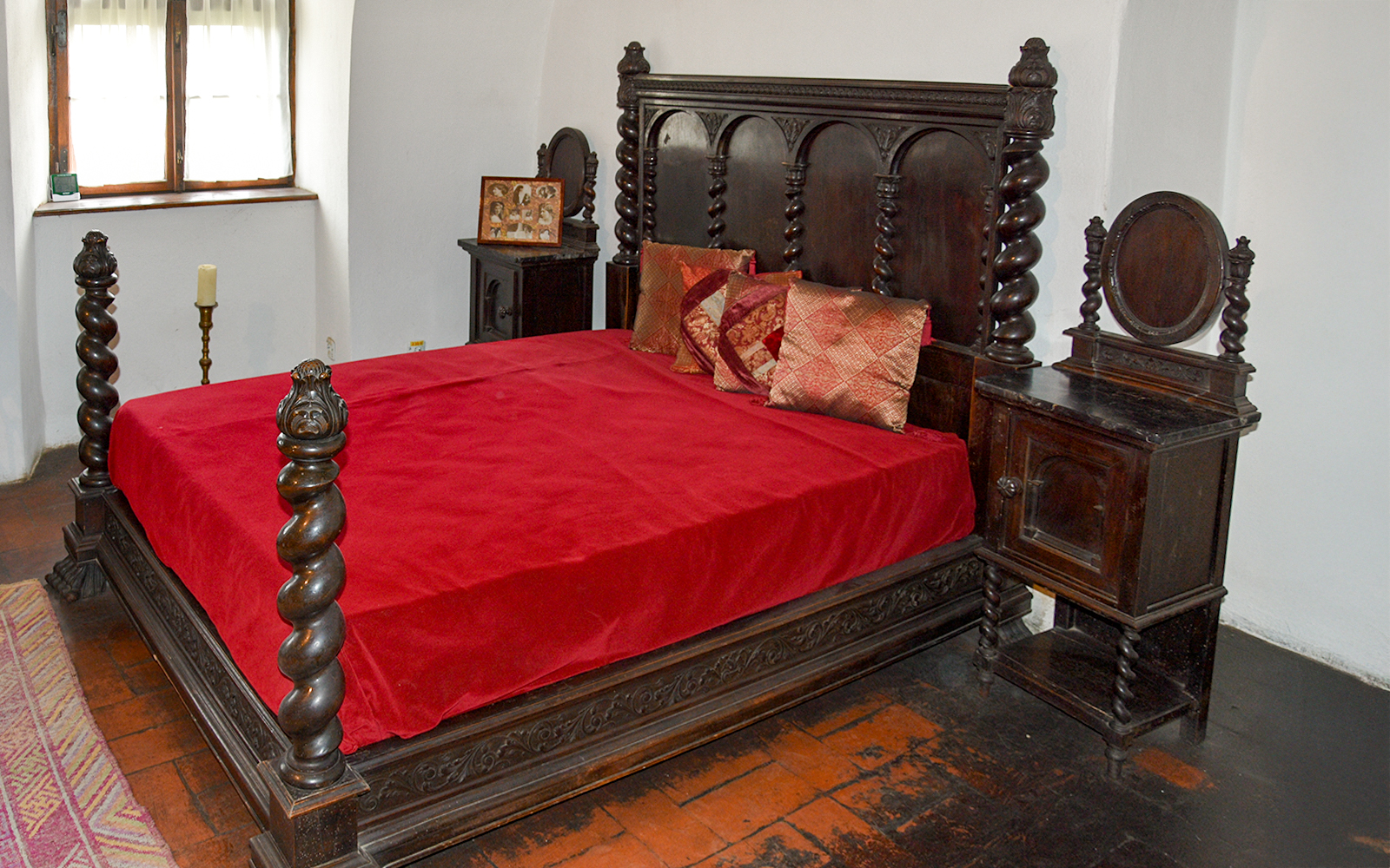 Wooden medieval bed in Bran Castle bedroom with red bedding.