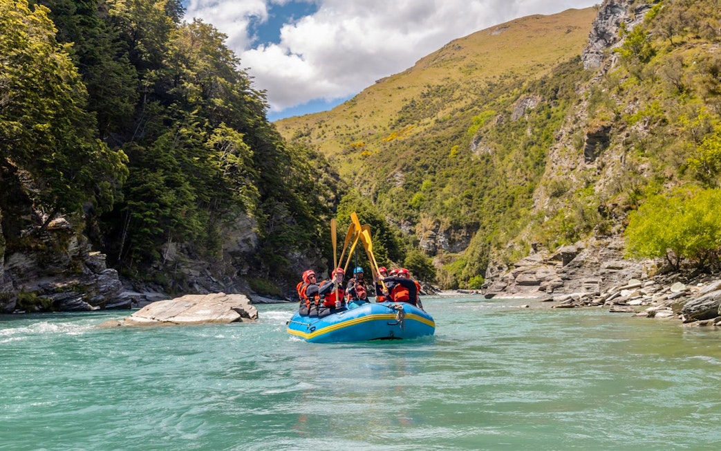 Whitewater rafting on Shotover River, Queenstown, with lush green cliffs in the background.