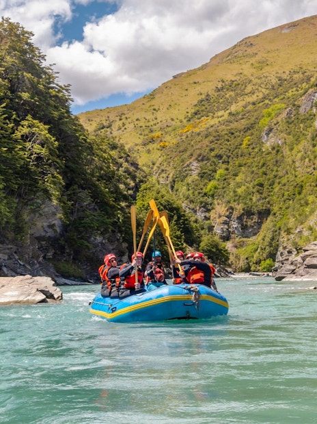 Whitewater rafting on Shotover River, Queenstown, with lush green cliffs in the background.