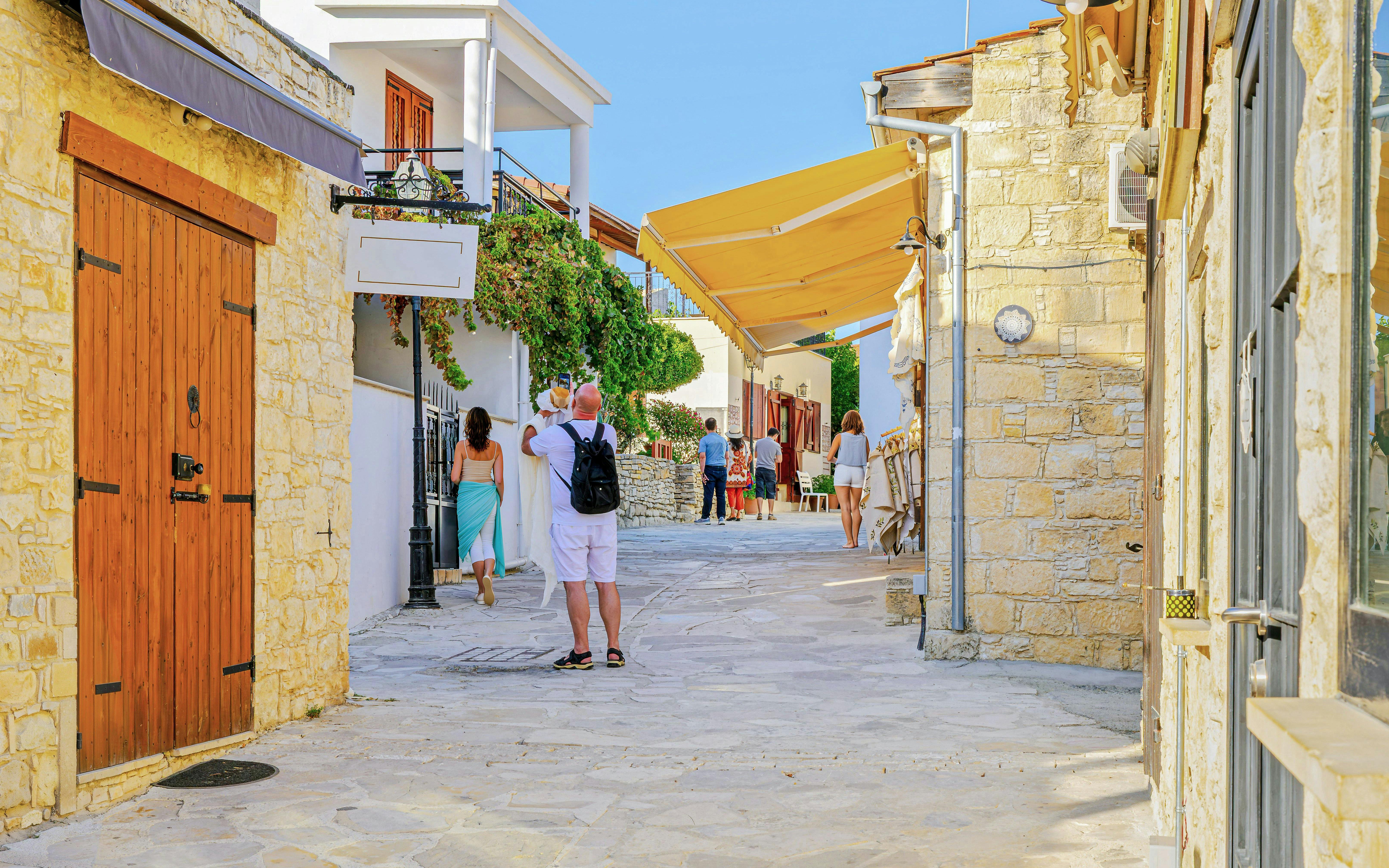 Tourists explore a narrow street in Omodos, Troodos Mountains, with stone buildings and shops.