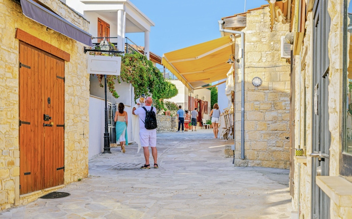 Tourists explore a narrow street in Omodos, Troodos Mountains, with stone buildings and shops.