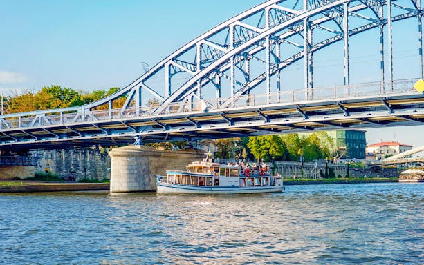 Boat cruising under a steel bridge on the Vistula River during a Cracow city tour.