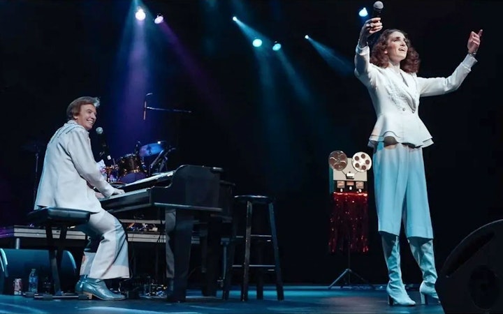Performers on stage during Carpenters Legacy show, with one playing piano and the other singing.