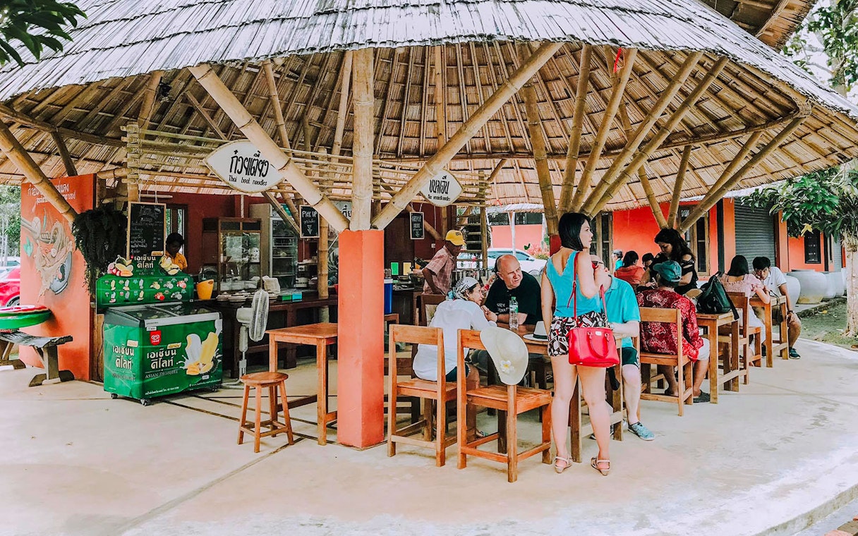 Outdoor dining area in Pita Village near the emerald pool, featuring a bamboo-roofed Thai noodle shop.