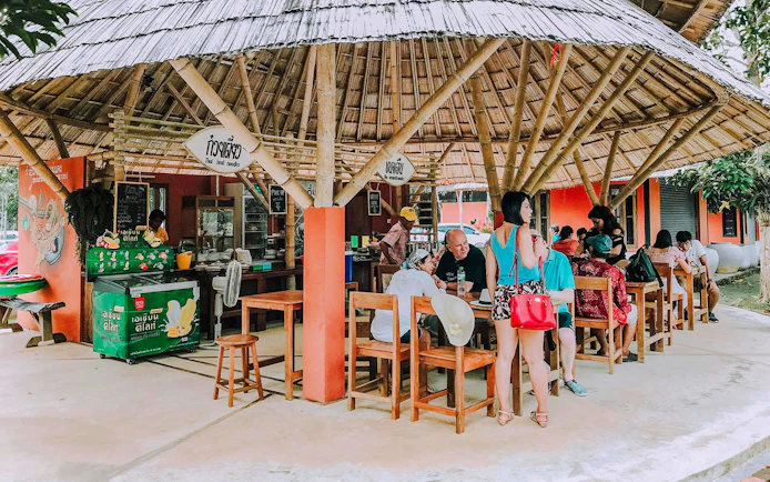 Outdoor dining area in Pita Village near the emerald pool, featuring a bamboo-roofed Thai noodle shop.