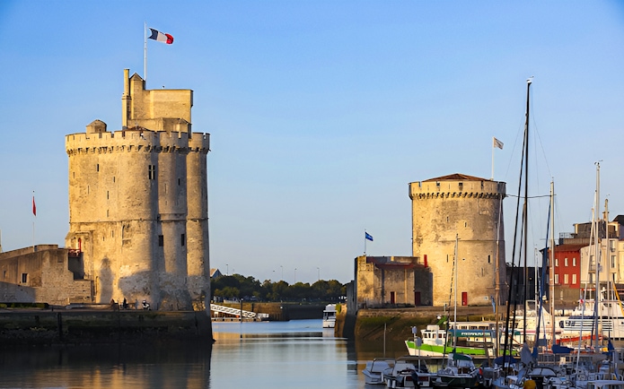 Towers of La Rochelle overlooking the harbor with boats docked nearby.