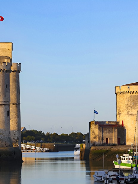 Towers of La Rochelle overlooking the harbor with boats docked nearby.