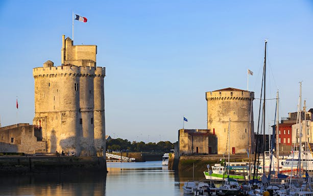Towers of La Rochelle overlooking the harbor with boats docked nearby.