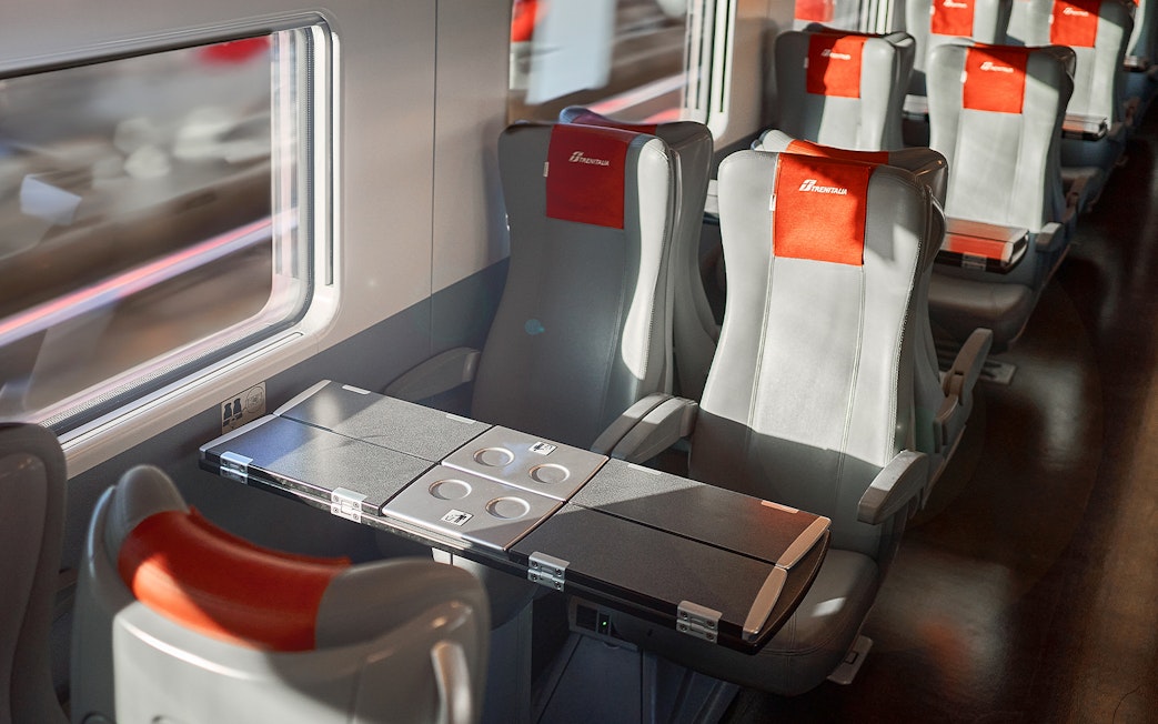 Trenitalia train standard class seats with foldable tables and window view.
