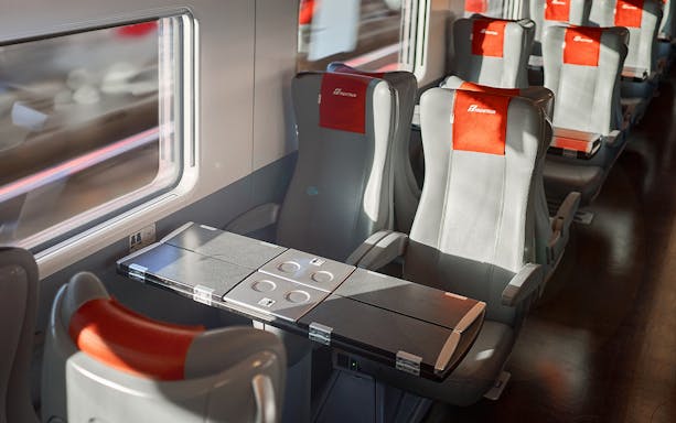 Trenitalia train standard class seats with foldable tables and window view.