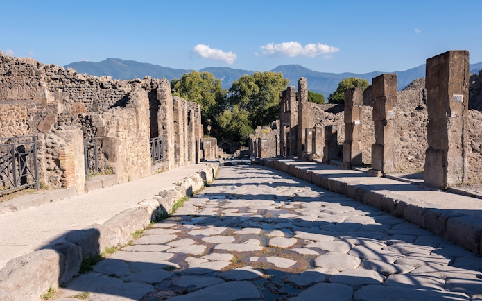 Ancient stone street in Pompeii with ruins and distant mountains.