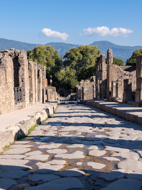 Ancient stone street in Pompeii with ruins and distant mountains.