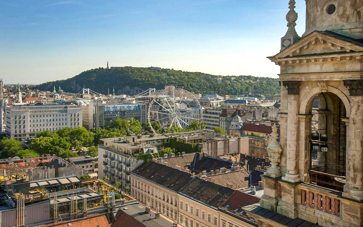 View of Budapest cityscape from St. Stephen's Basilica, featuring a Ferris wheel and Gellért Hill.