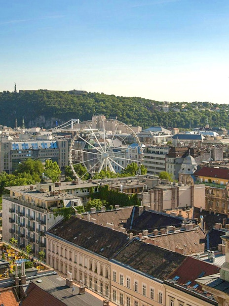View of Budapest cityscape from St. Stephen's Basilica, featuring a Ferris wheel and Gellért Hill.
