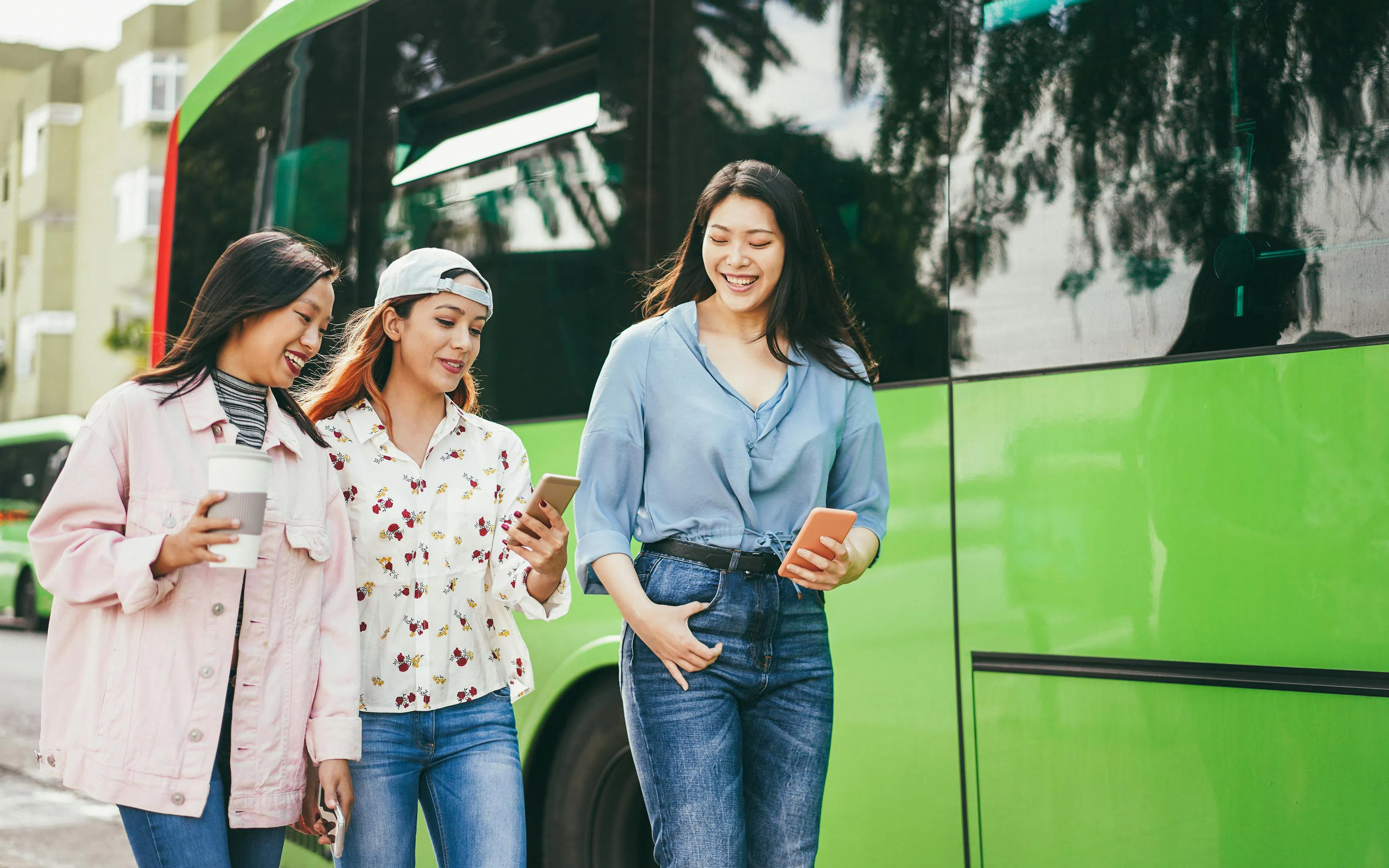 Tourists using phones near a green bus at a Shenzhen station.