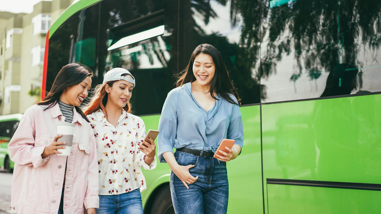 Tourists using phones near a green bus at a Shenzhen station.