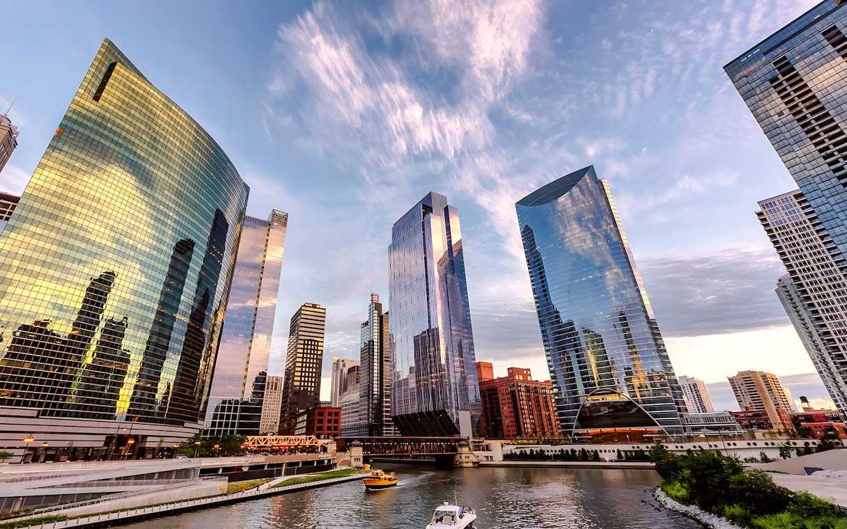 Chicago skyline with modern skyscrapers reflecting sunset colors over the river.