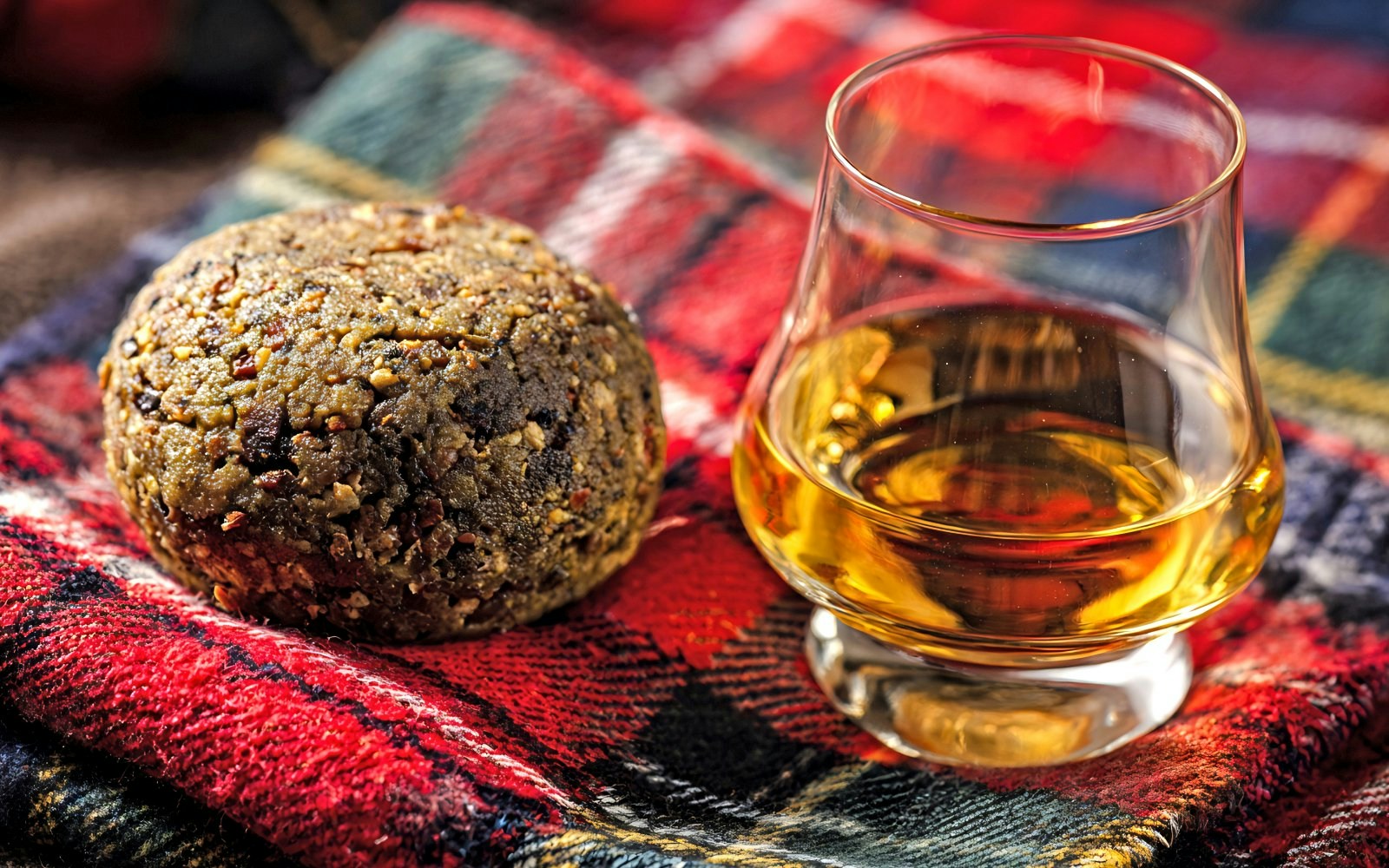 Scottish haggis and whisky glass on tartan cloth.