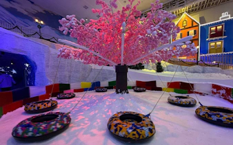 Snow-covered playground with swings and a pink tree at Genting Highlands Snow World Theme Park.