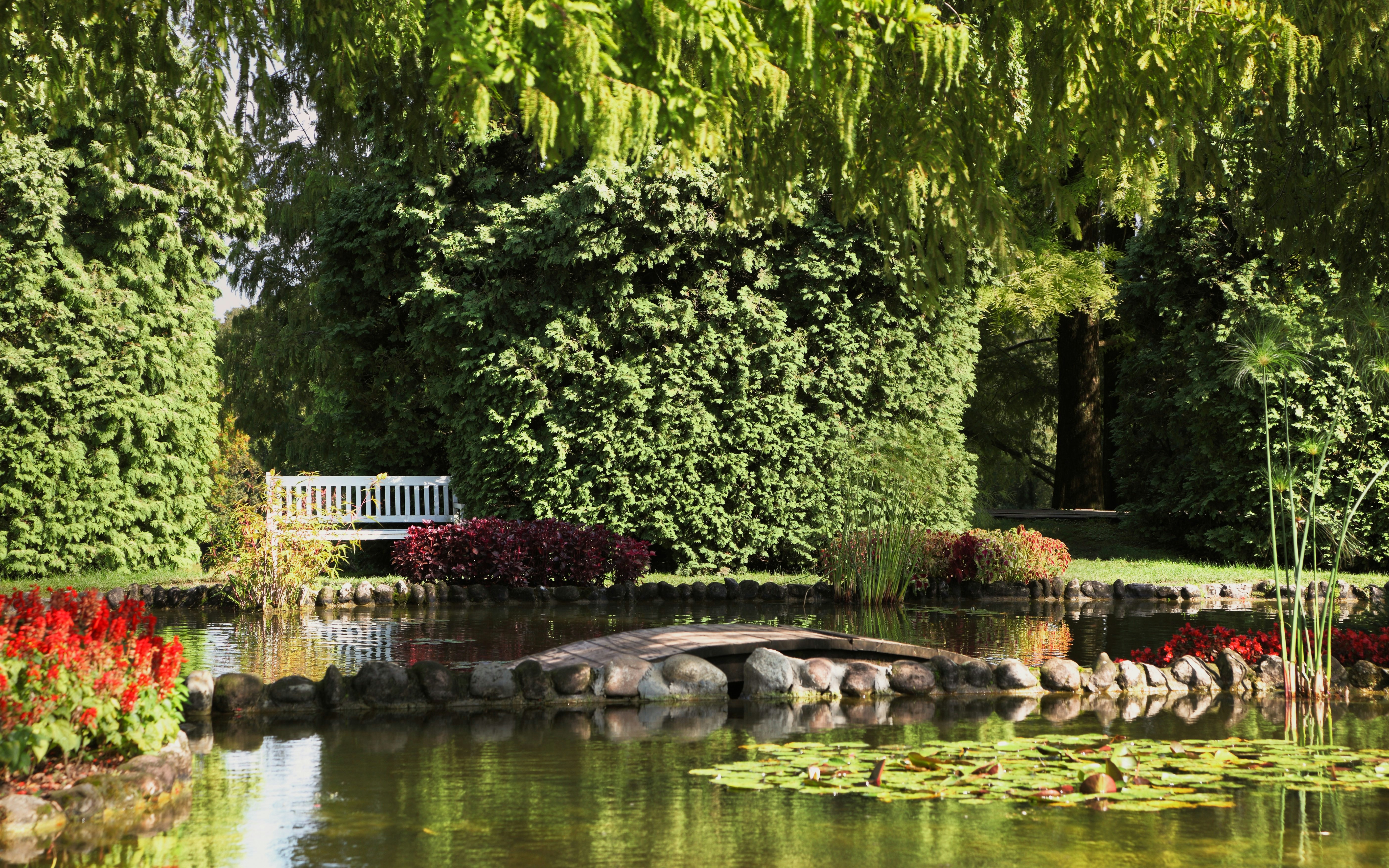 Sigurta Garden pond with stone bridge, surrounded by lush greenery and vibrant flowers.