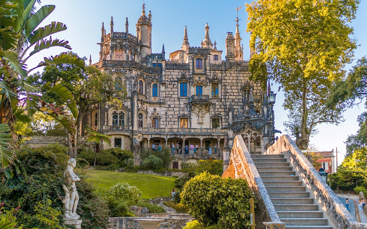 Quinta da Regaleira exterior with ornate architecture, garden, and stone staircase in Sintra, Portugal.