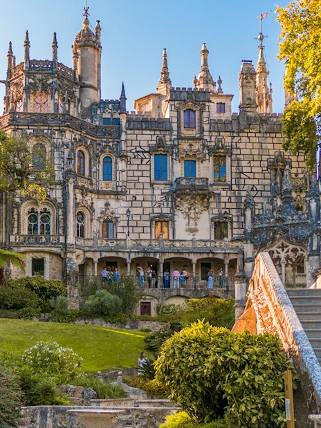 Quinta da Regaleira exterior with ornate architecture, garden, and stone staircase in Sintra, Portugal.