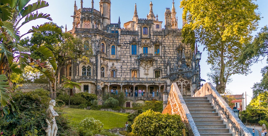 Quinta da Regaleira exterior with ornate architecture, garden, and stone staircase in Sintra, Portugal.